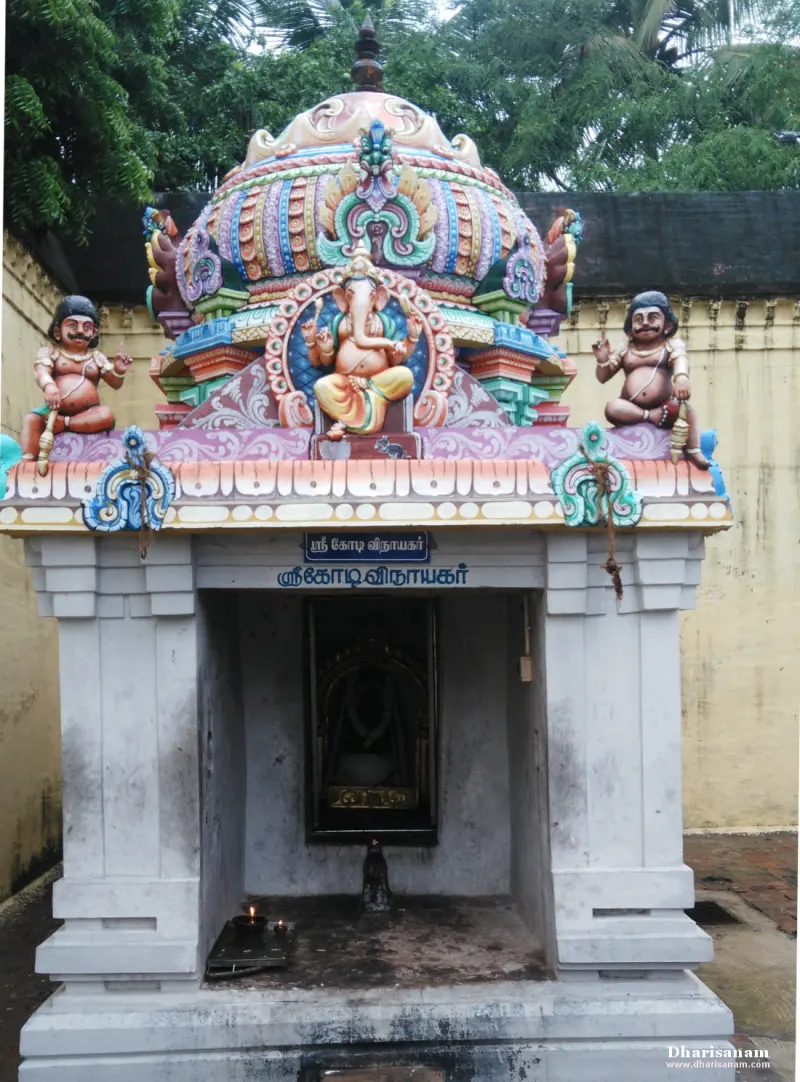 A small white shrine with a colourful roof, a seated Vinayakar on top, and a blue name board