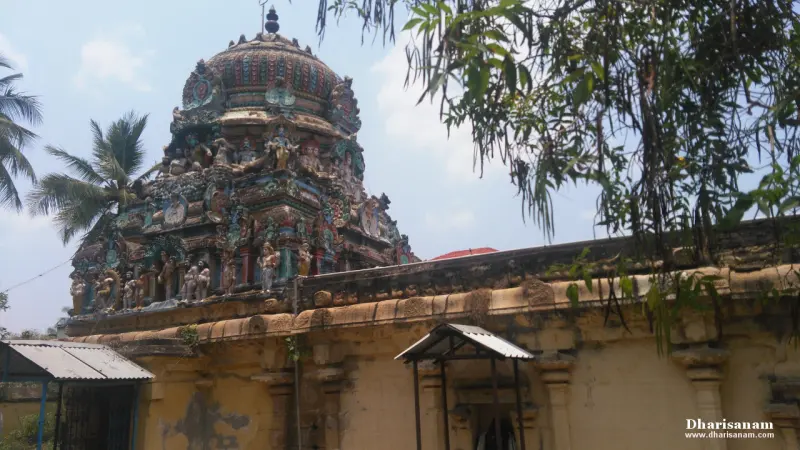 A domed tower with painted sculptures above a yellow wall, with trees around.