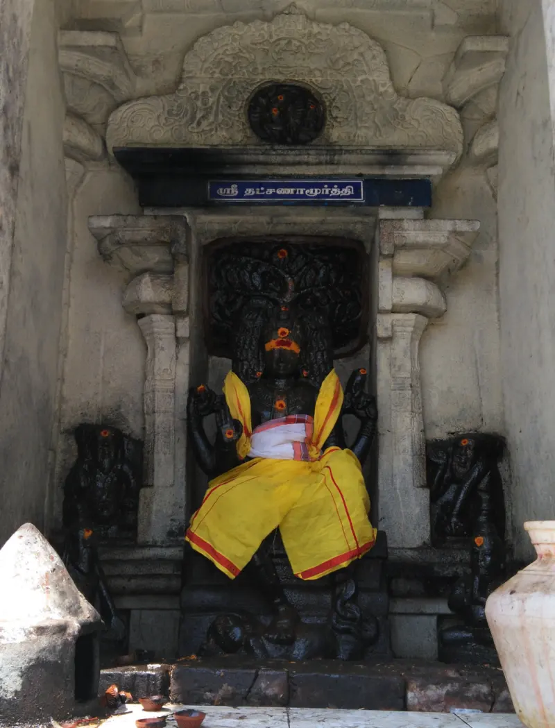 Black stone Dakshinamurthy seated in a niche, wearing a yellow cloth