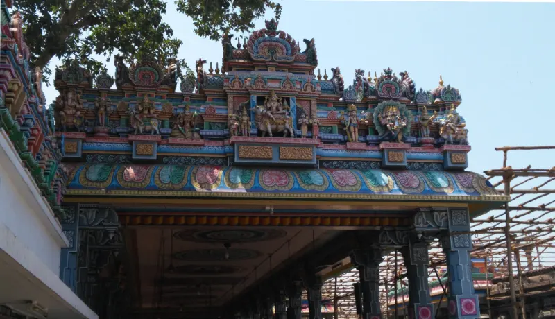 The ornate front of a porch roof, covered with painted figures, above carved stone pillars.