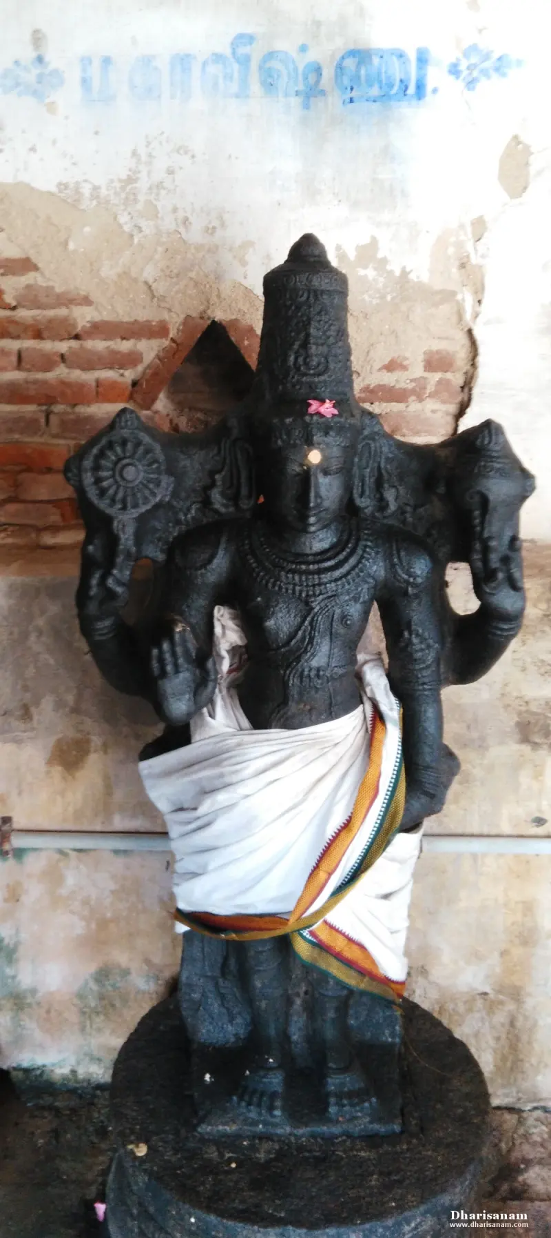 A standing four-armed black stone idol with a tall crown and a wheel in one hand; a Tamil label above names Mahavishnu.