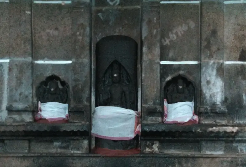 Three dark stone figures in wall niches, each wrapped at the waist in white cloth with a red border.