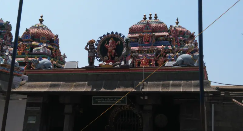 A shrine front with a roof of painted figures, a ring-shaped sculpture in the centre, and a dark doorway below.