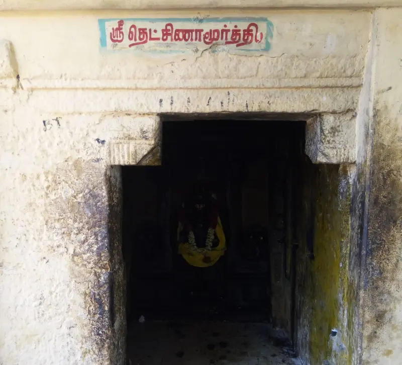 Whitewashed shrine doorway under a Tamil name board, with a garlanded image inside