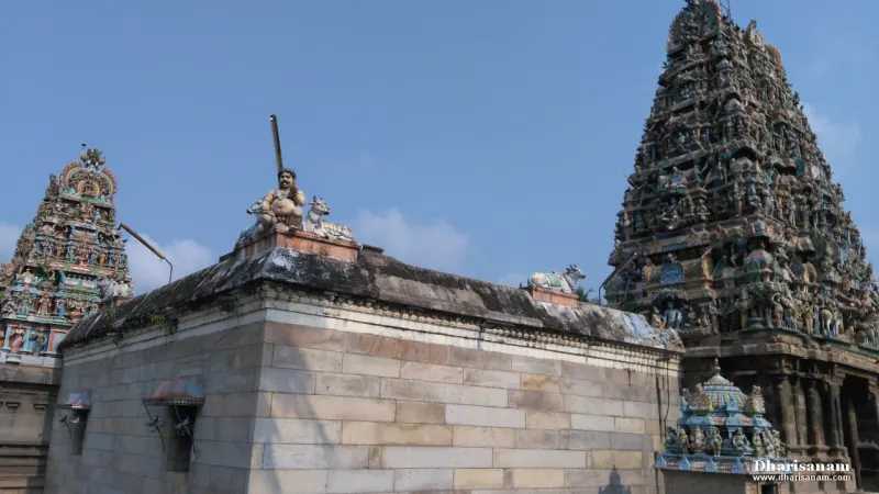 A stone shrine roof with a seated figure and bulls on top, and two painted temple towers rising behind it