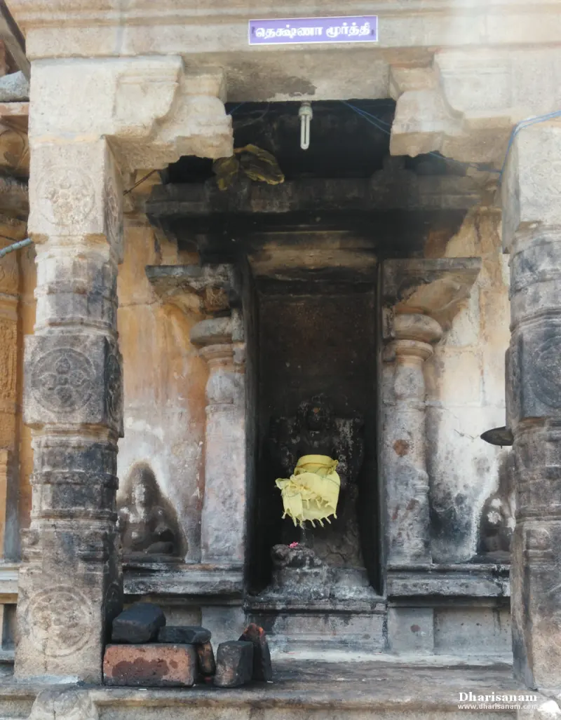 Weathered stone niche with a small idol covered with a yellow cloth and a name board above it