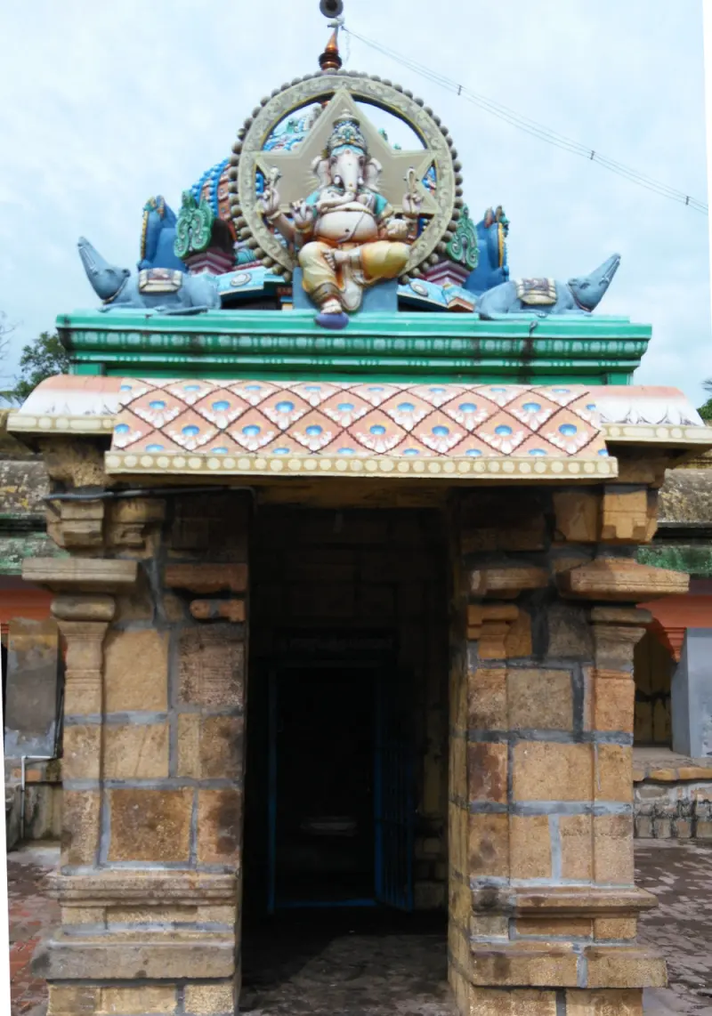 A small stone shrine with a coloured Vinayakar figure and two mice on its roof, and a dark doorway below.