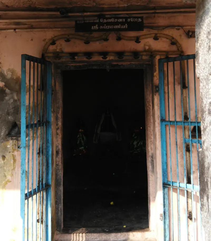 Dark shrine doorway with a name board for Murugan, with two consorts, and blue iron gates