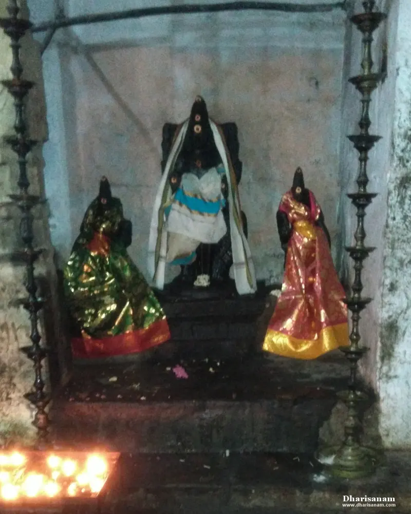 A central seated idol with two idols dressed in bright silk on either side, between tall brass lamps.