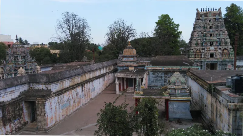Aerial view of a temple courtyard with tiled-roof shrines, long walls and a gopuram behind