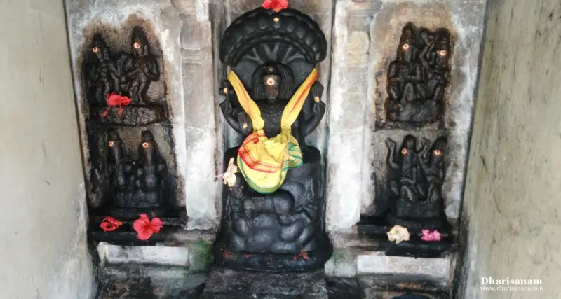 A dark stone idol beneath a hooded canopy in a yellow cloth, between carved panels with flowers.