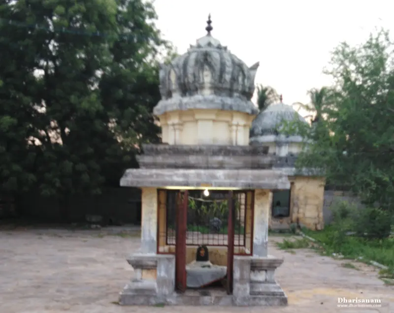 A small domed shrine in an open courtyard with a lingam behind an iron grille