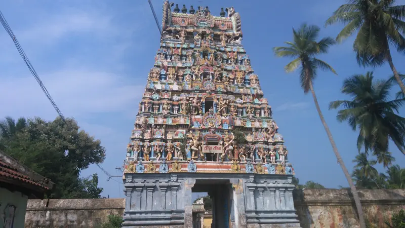 A tall gateway tower covered in coloured figures, with coconut palms beside it