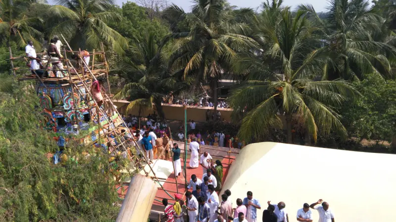A painted tower wrapped in bamboo scaffolding, with workers on top and a crowd gathered below.
