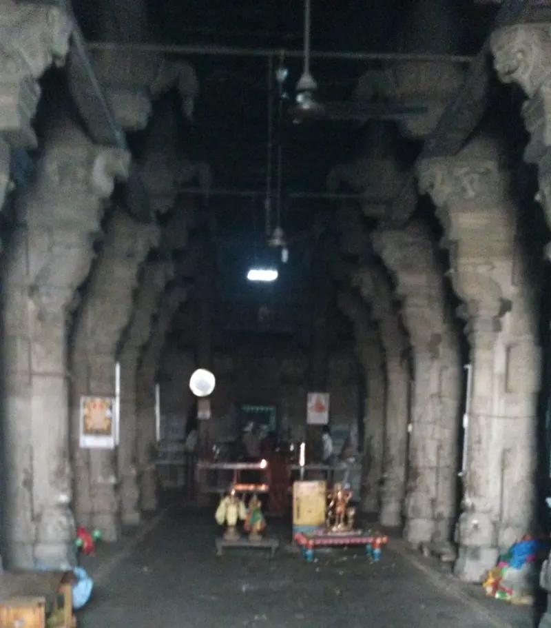 A dim hall with rows of heavy stone pillars leading to a lit altar area at the far end