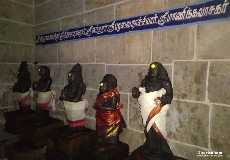 Five black stone idols in a row below a long blue Tamil name board