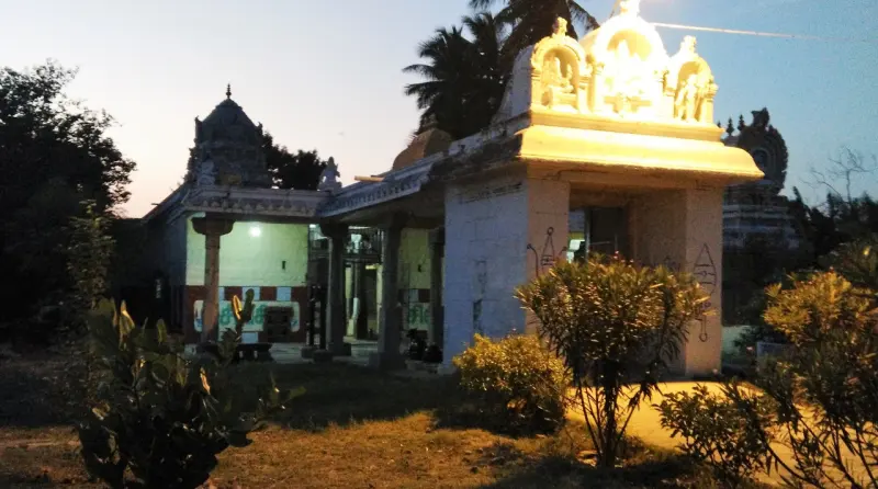 A porch with a sculpted roof in front of a pillared corridor, with bushes in the foreground.