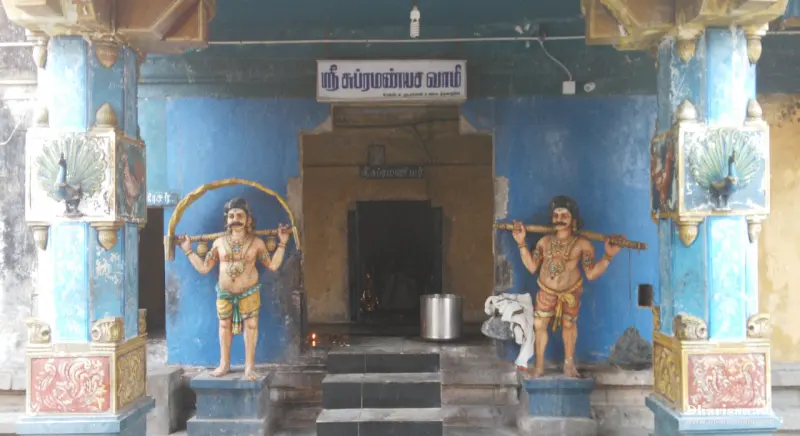 A blue-walled shrine with peacock reliefs on the pillars and two painted figures carrying poles at the entrance
