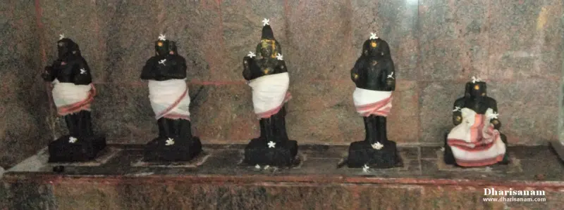 Five small black stone idols wearing white cloths, with flowers at their feet