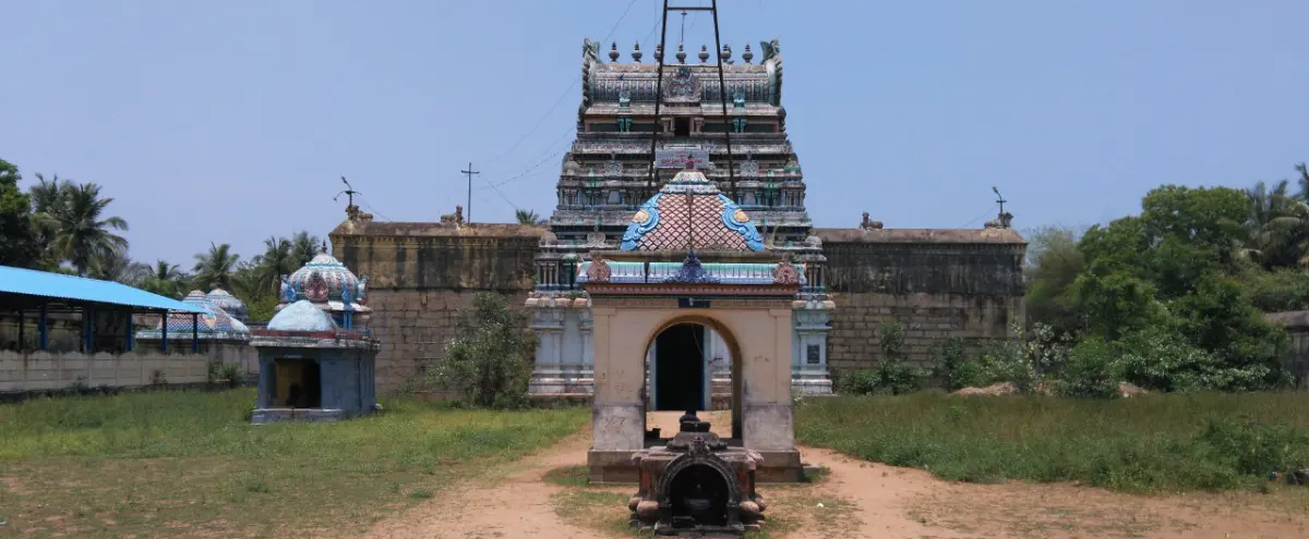 The tiered Rajagopuram rises behind a small shrine with an arched doorway; grass and palms line the open ground.