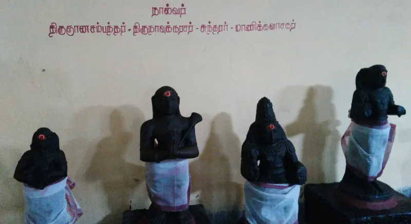 Four dark idols in white cloth before a wall with the names of the four saints painted above.