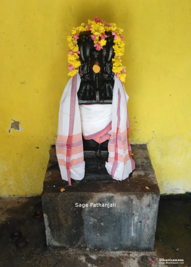 A black stone figure of Sage Pathanjali with a yellow and pink flower garland and a white cloth, on a stone base