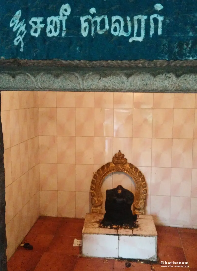 Small black idol under a golden arch beneath a Tamil name board