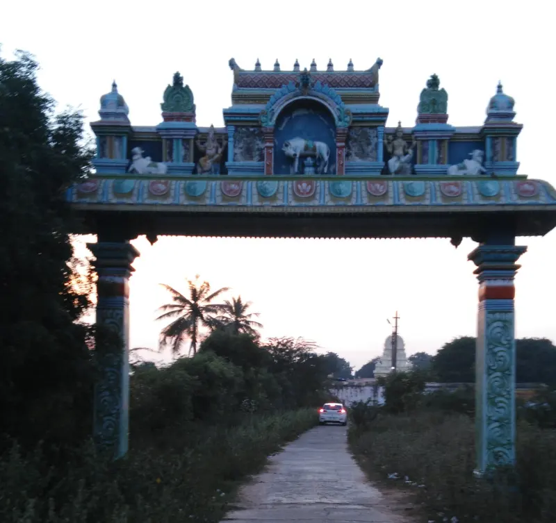 A painted arch with a bull and deity figures over a narrow road, with a temple tower in the distance.