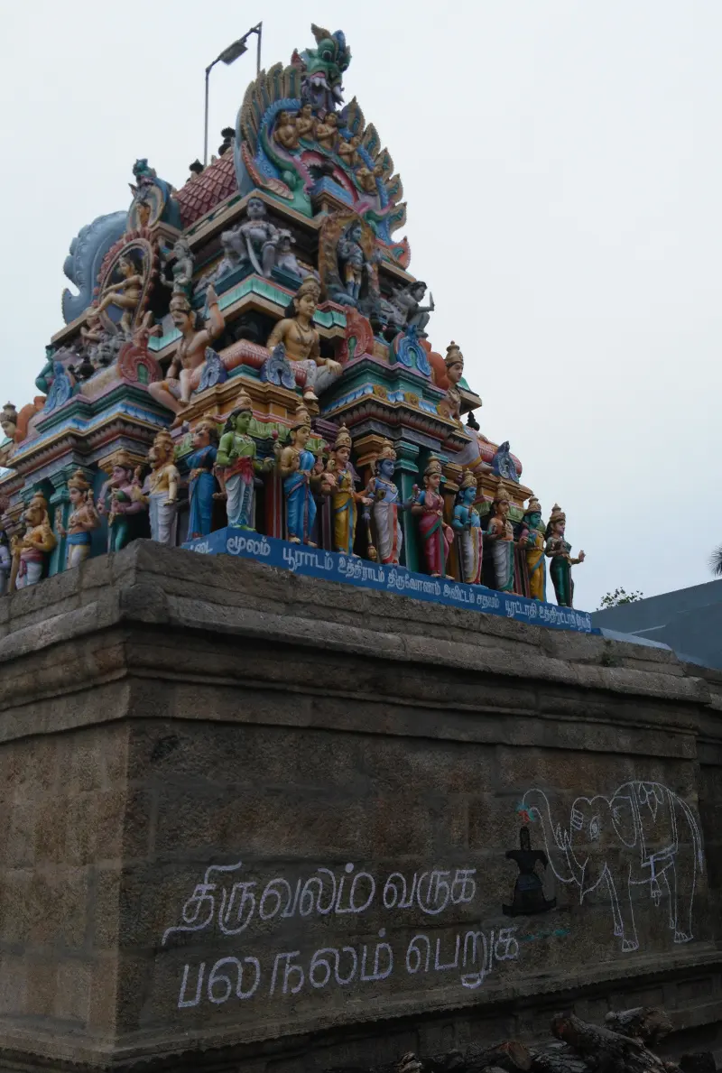 A tower of painted figures above a stone wall with Tamil words and a drawn elephant