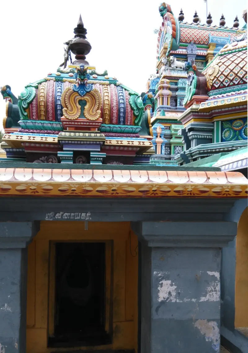 A small shrine with a painted dome and a Tamil name board reading Vinayakar, with a dark doorway below