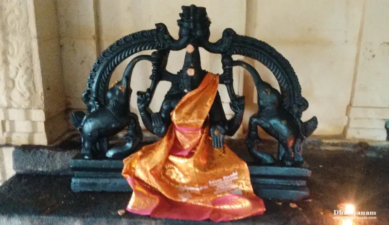 A black stone idol seated under an arch, with an elephant on each side and an orange silk cloth draped over it.