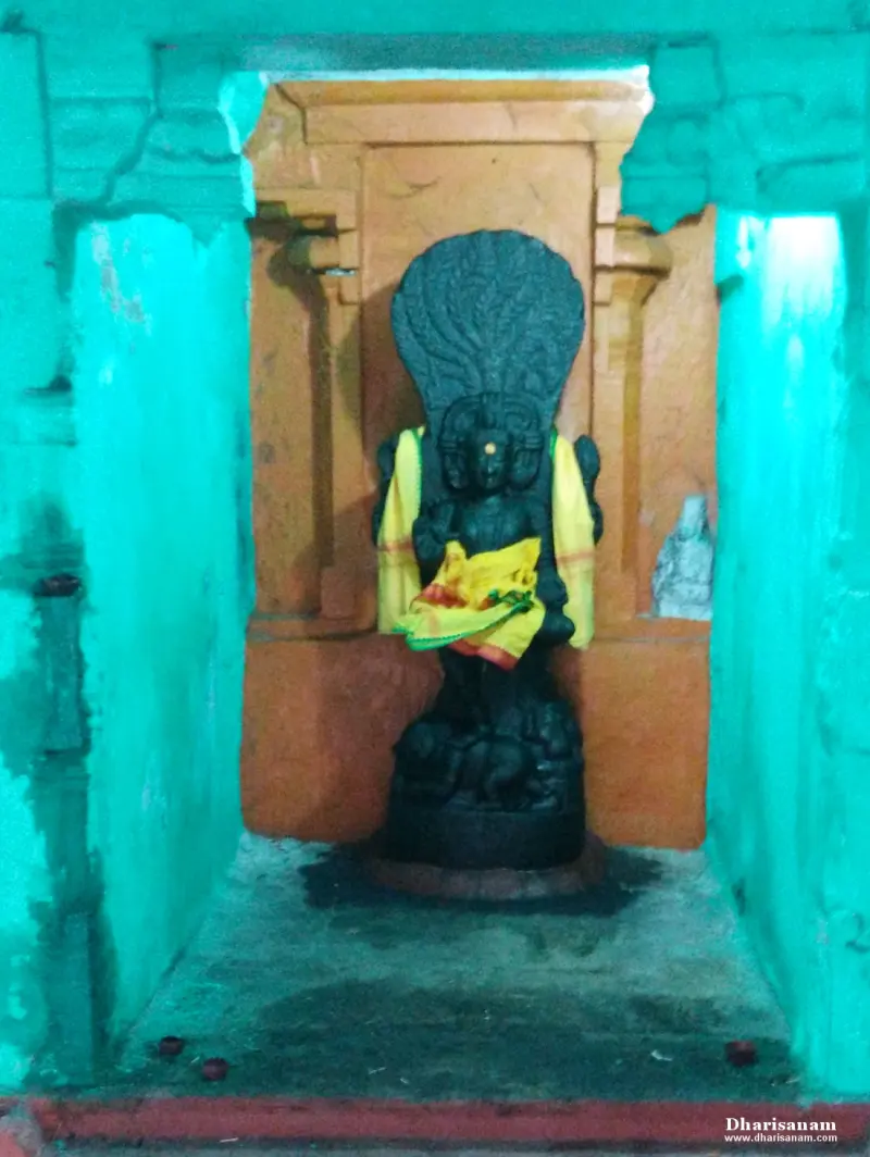 Dark idol with a spread hood, draped in yellow cloth, in a small green and orange shrine