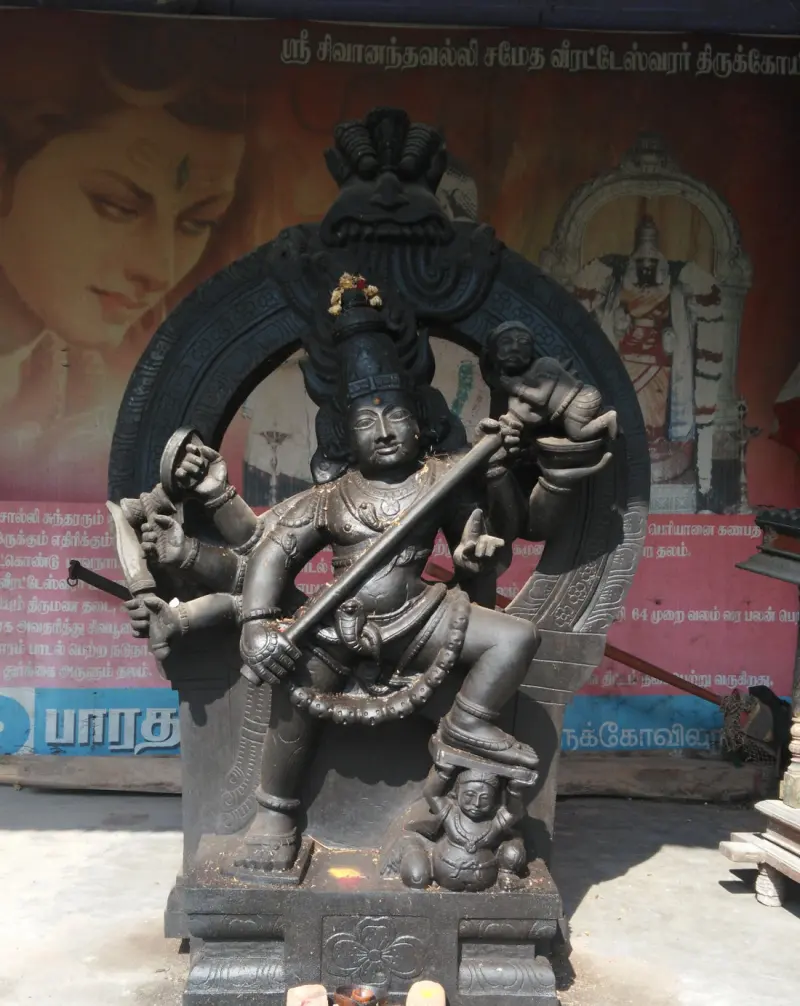 A dark stone figure with many arms holding a trident, a small demon figure at the top and another under his foot