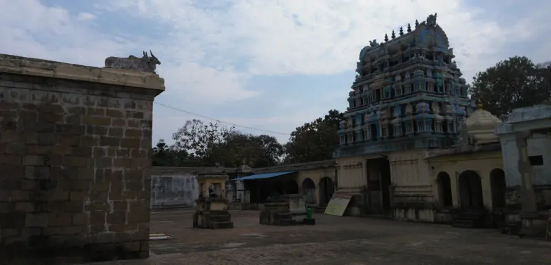 A tall gopuram rises behind a stone wall and an open courtyard