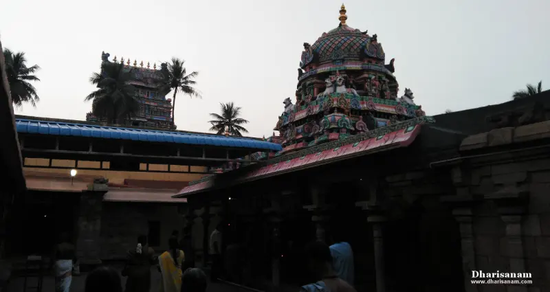 A colourful domed shrine roof above a dark corridor, with devotees below and a gopuram beyond