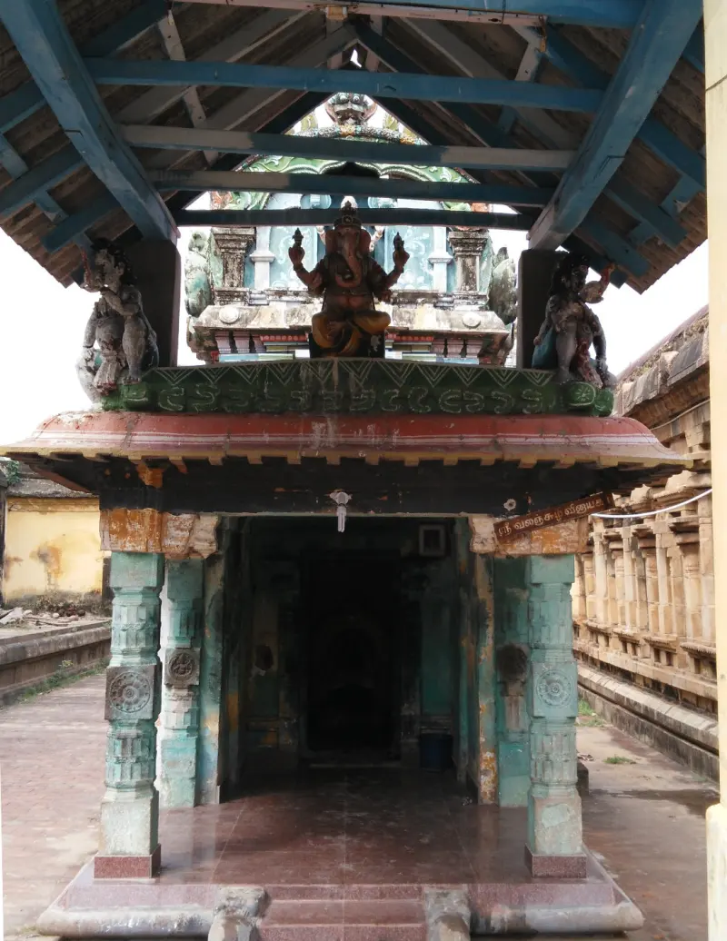 A stone porch with green pillars and a tiled roof; a painted Vinayakar figure sits above the dark entrance.