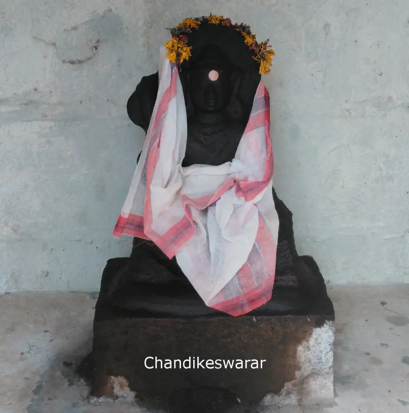 A dark idol with flowers and a white cloth, labelled Chandikeswarar