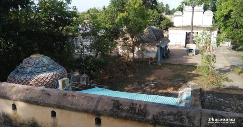 View over the compound wall to a courtyard with trees, a patterned dome and small shrines