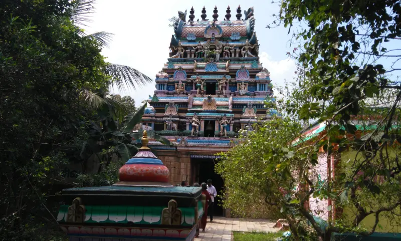 A multi-tiered tower covered in painted figures, with a small shrine roof in front and trees around