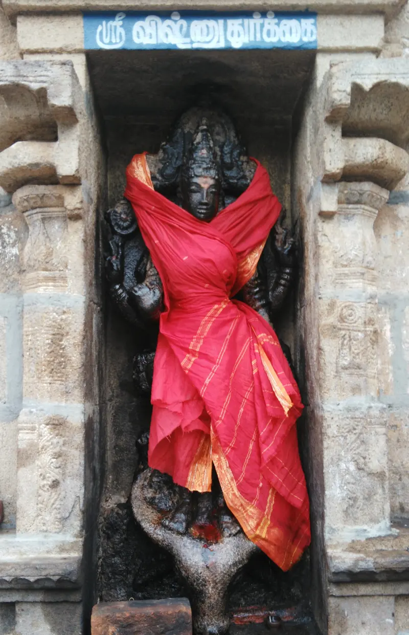 Dark stone goddess draped in red cloth, in a niche under a blue Tamil name board
