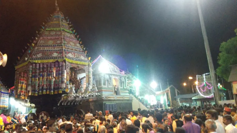 A large temple chariot lit at night among a crowd