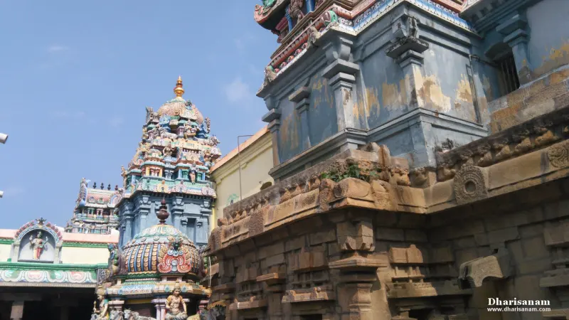 Painted shrine towers behind an old carved stone wall in the temple, seen against a blue sky