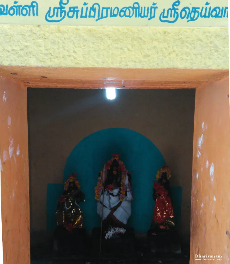 Three garlanded dark stone figures in a small shrine under a Tamil name board, the central one the tallest
