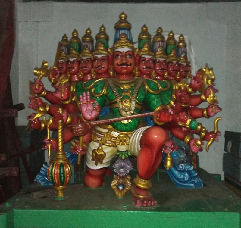 A seated painted figure with many heads and arms, holding weapons, on a green platform.