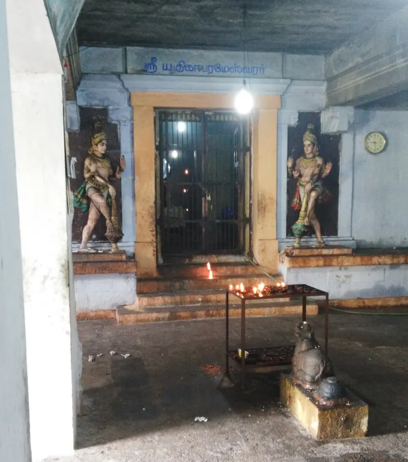 A shrine doorway with a guardian figure on each side and lamps lit on the steps