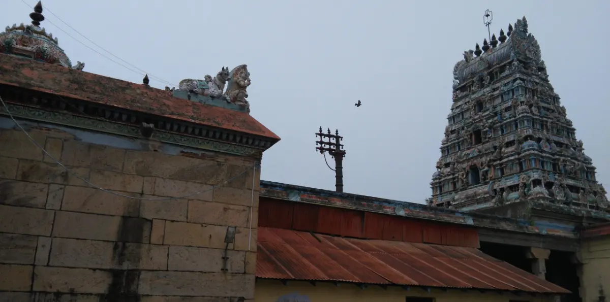 Tiled temple roof and a tall carved tower rising behind a stone wall under a grey sky.