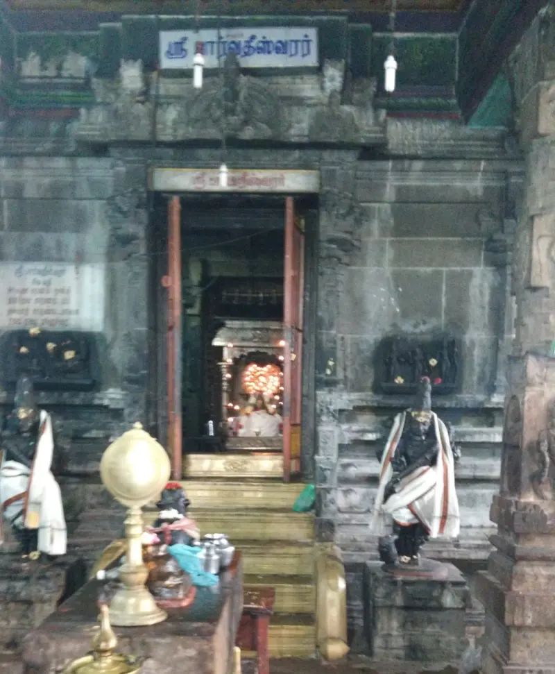 Stone doorway with a name board, steps, a brass lamp stand and a guardian figure on each side.