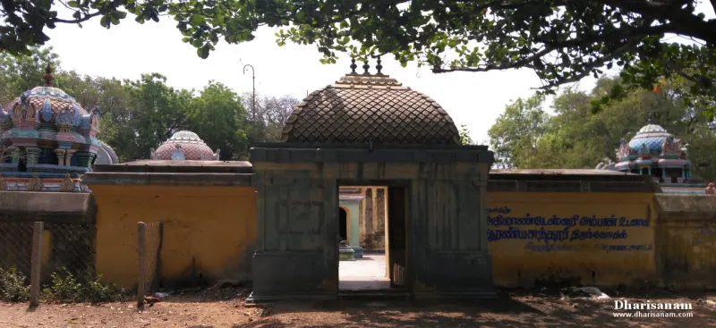 Stone gateway with a domed top in a yellow wall, with Tamil writing on the wall at right