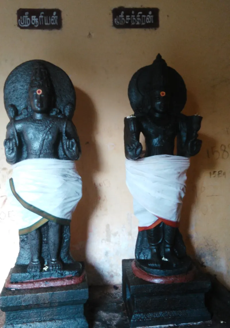 Two black stone idols side by side in white cloth, labelled in Tamil as Suryan on the left and Chandran on the right.