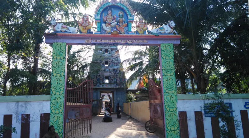 Green-pillared arch topped with painted figures, with the gopuram beyond